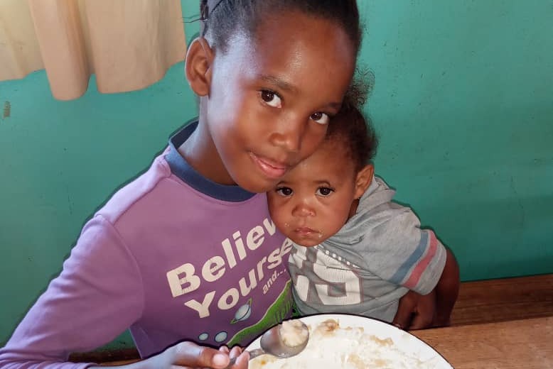 Zwei kleine Kinder sitzen vor einem Teller mit einer Mahlzeit